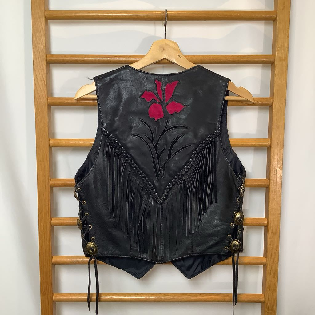 Black leather vest with red floral design and fringe on a wooden hanger against a white wall.