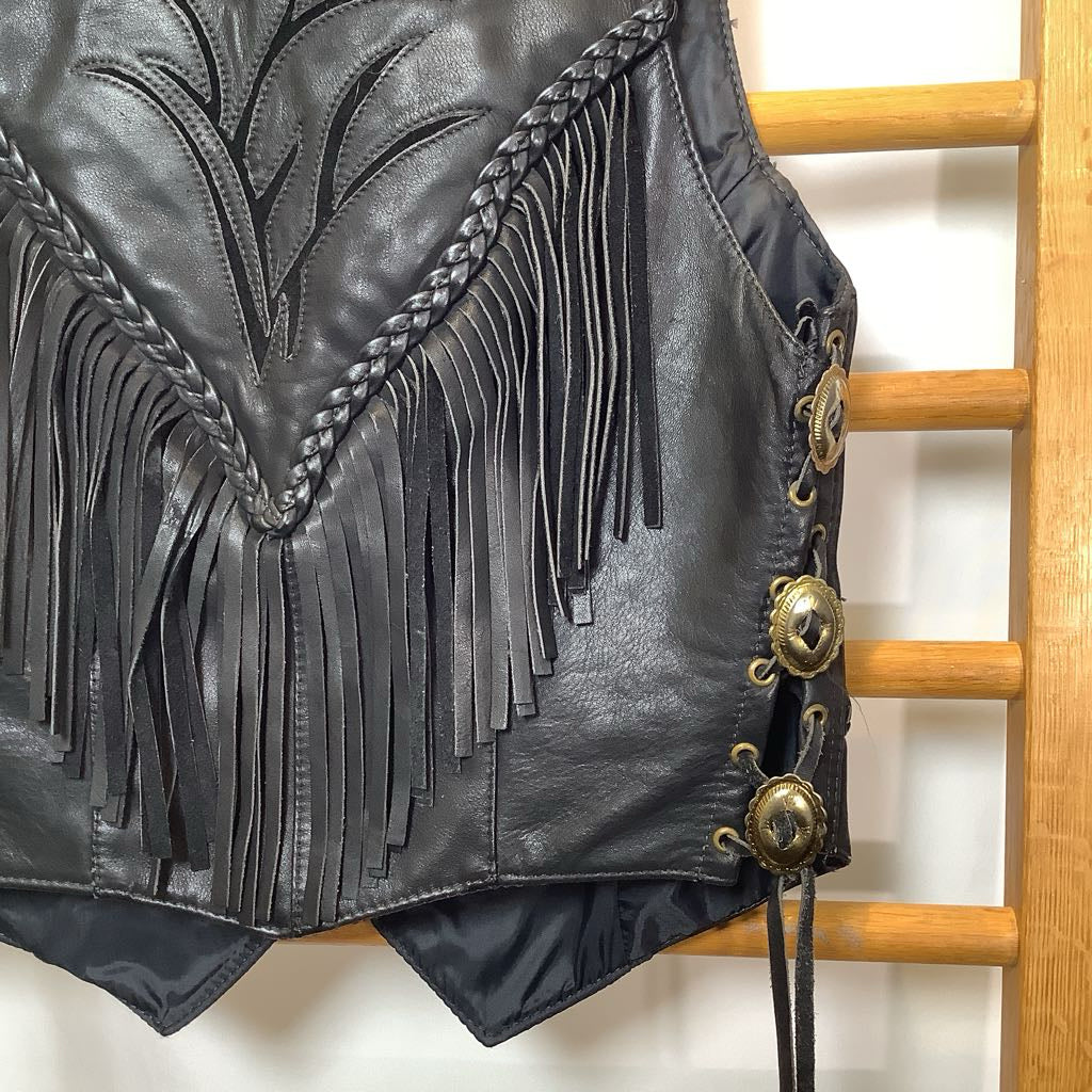 Black leather fringe jacket with gold buttons on a wooden rack.