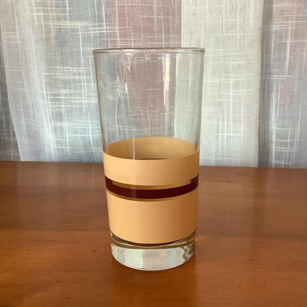 Clear glass with a beige striped band on a wooden surface and plaid curtain background