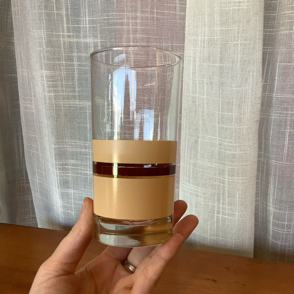 Clear glass with beige band held by a hand against a light curtain background
