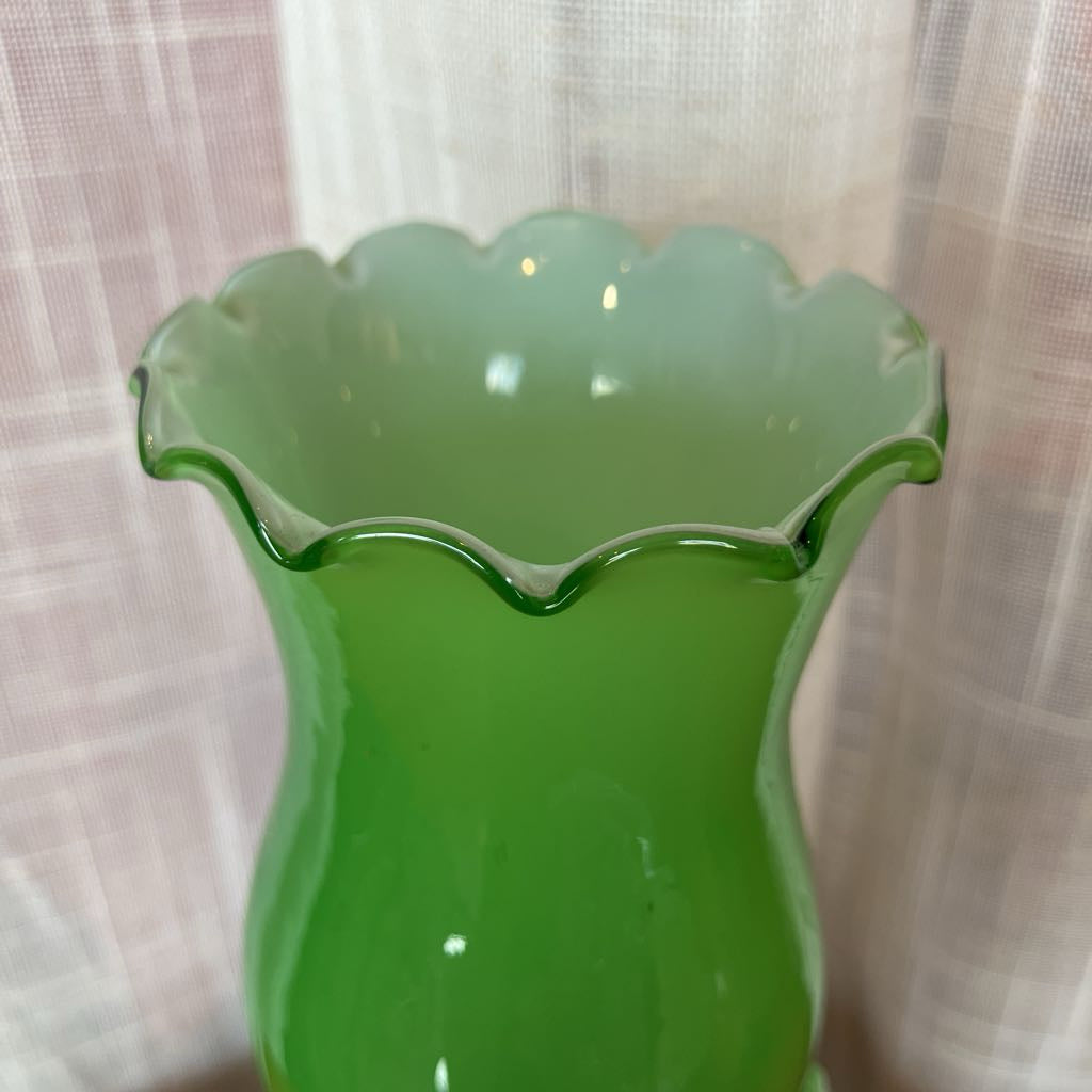 Green glass vase with scalloped edge against a neutral background