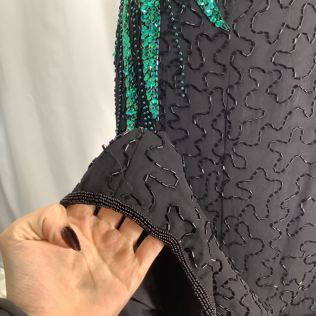 Close-up of a black garment with green embellishments held by a hand against a white background