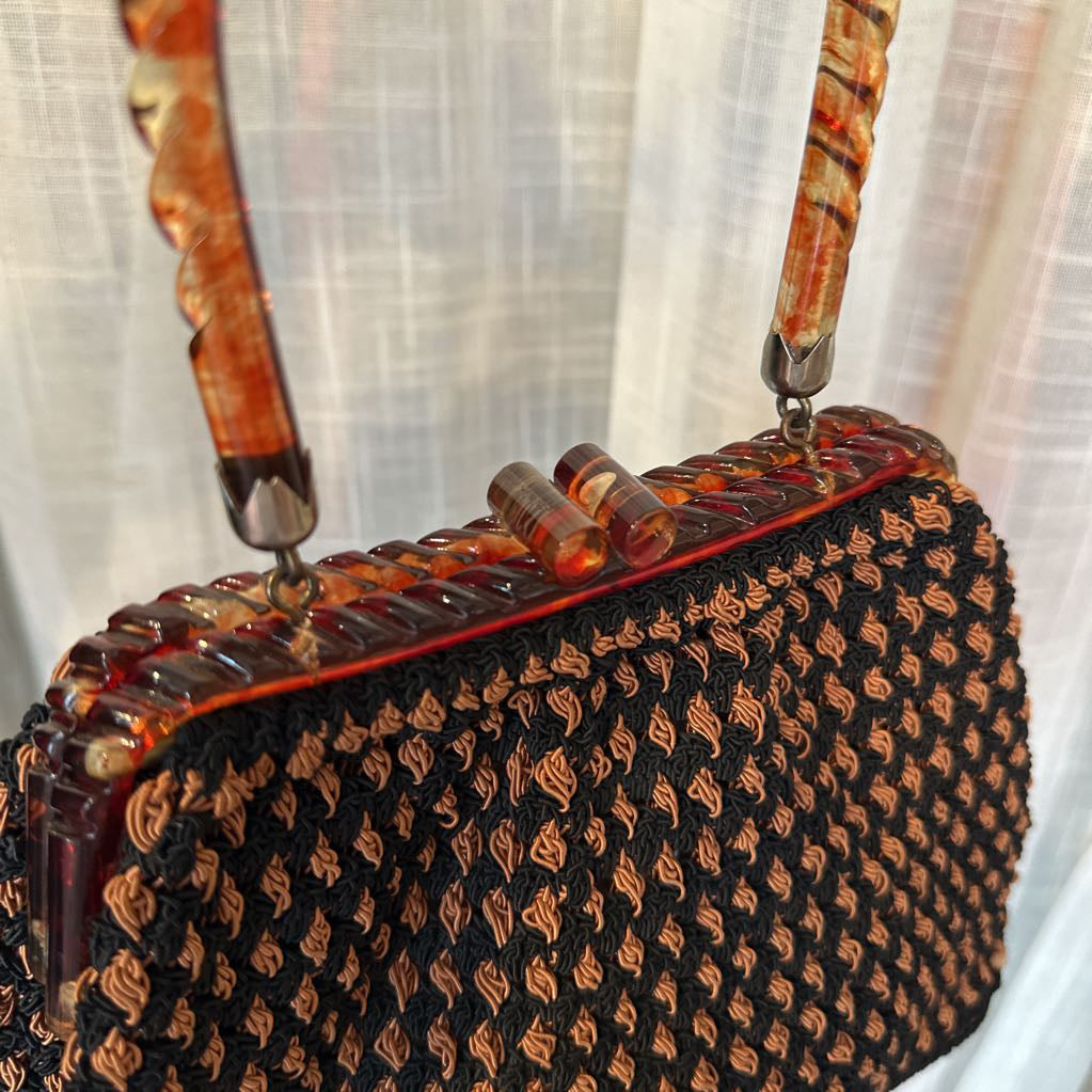 Handbag with intricate design and patterned handle against a neutral background