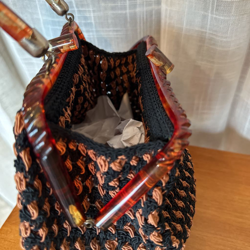 Black and brown woven bag with glass bottles inside, on a wooden surface.