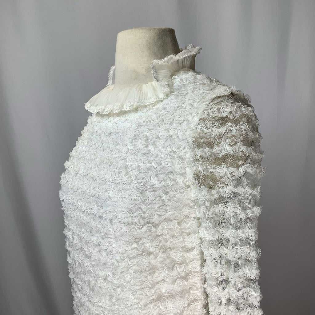 Mannequin wearing a textured white garment with ruffled details against a plain background