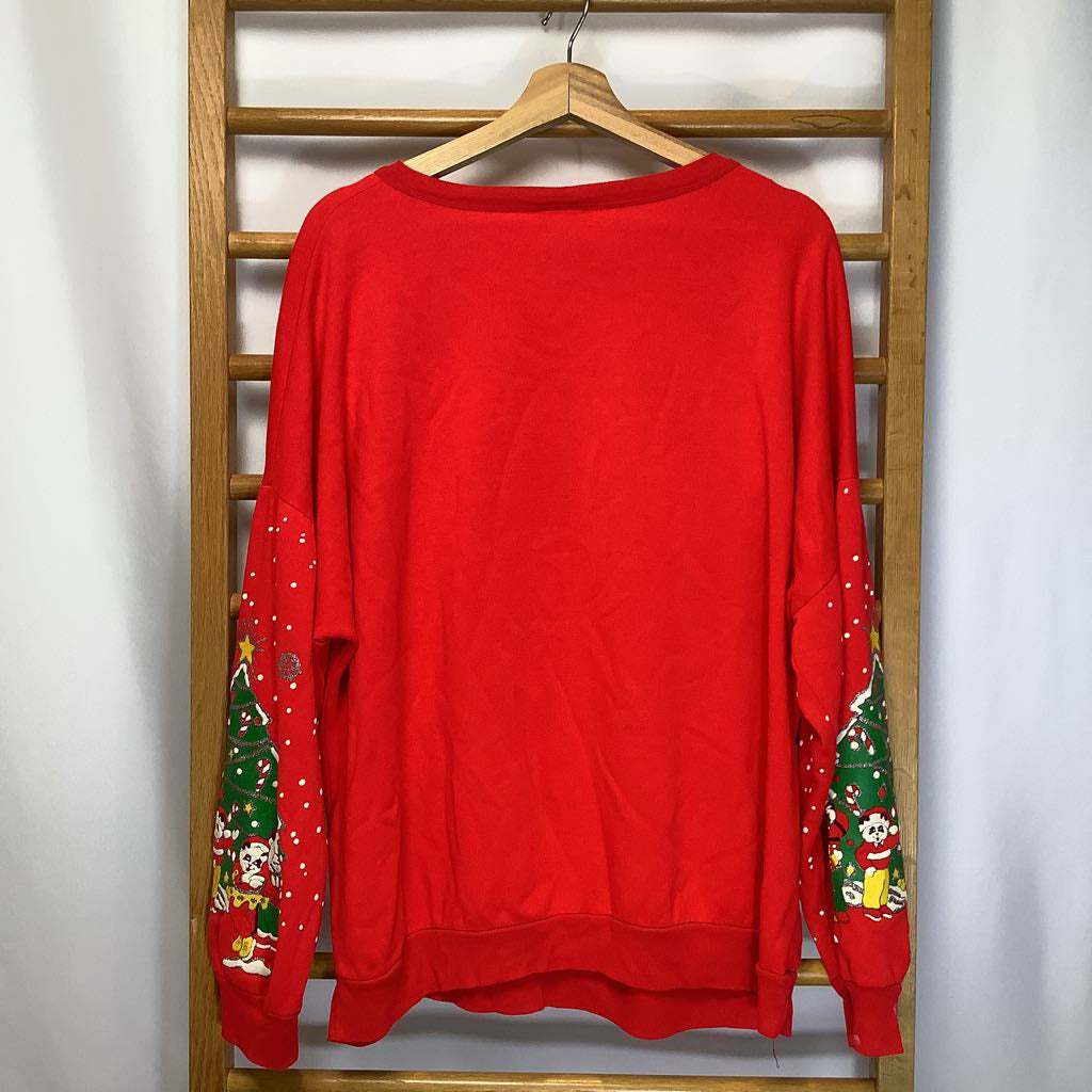 Red sweater with Christmas tree and Santa Claus designs on a wooden hanger against a white wall.