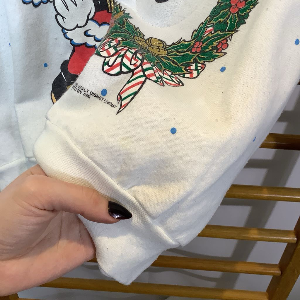 White sweatshirt with a colorful graphic design held by a hand on a wooden rack.