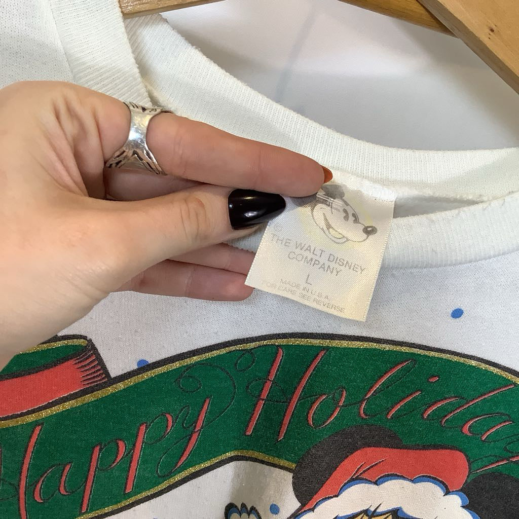 Hand holding a tag on a Disney holiday-themed shirt with 'Happy Holidays' text.