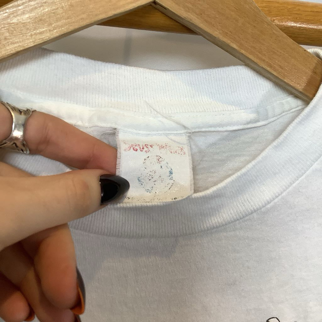 Close-up of a white shirt with a label being held by a hand, on a wooden hanger.