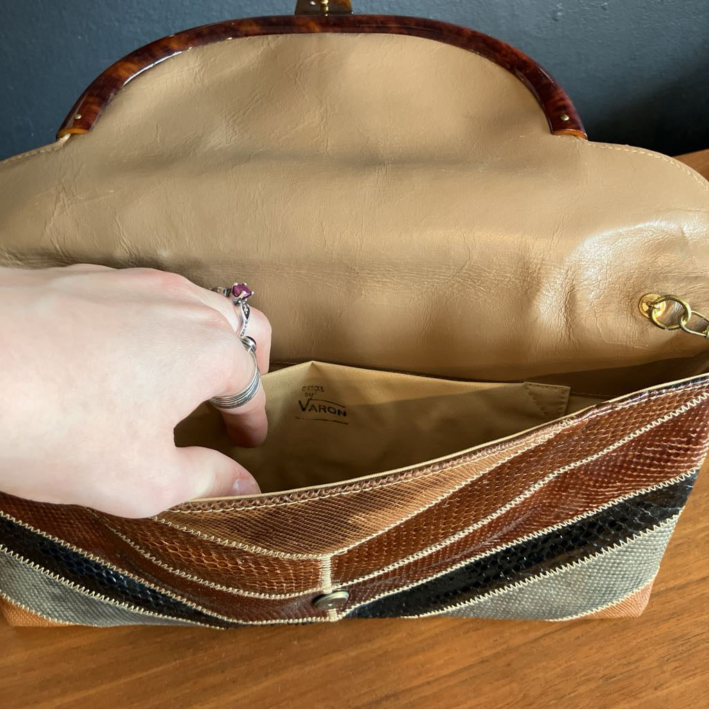 Hand opening a tan leather handbag with a visible brand name on a wooden surface.