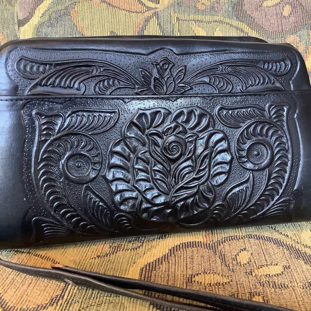 Black leather clutch with intricate floral embossing on a patterned surface