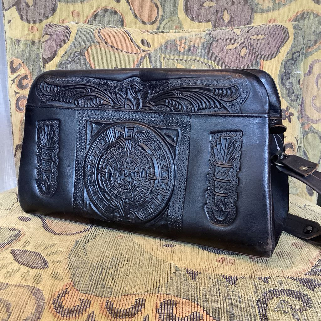 Black leather clutch with intricate designs on a patterned fabric background