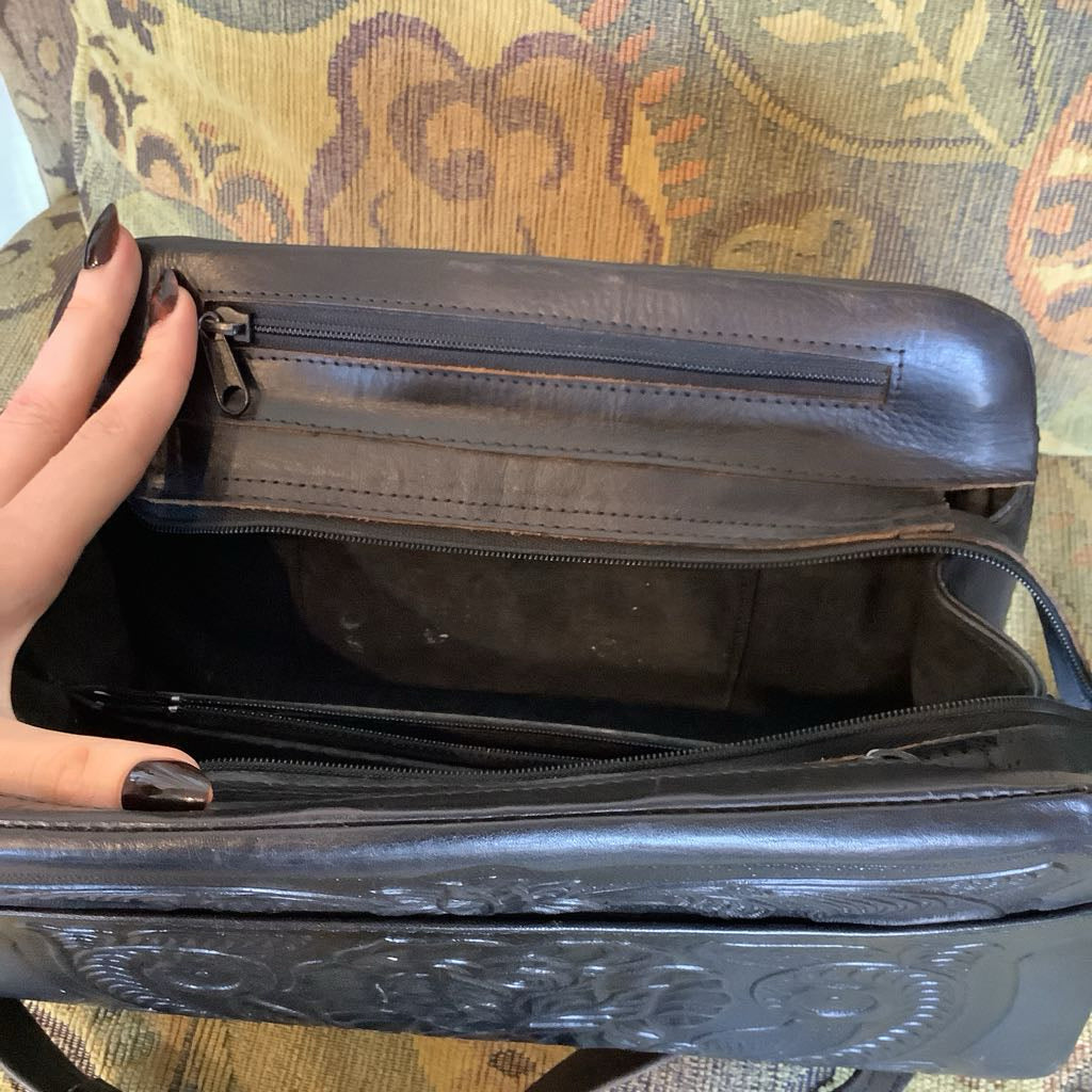 Black leather bag with a hand opening it on a patterned fabric background