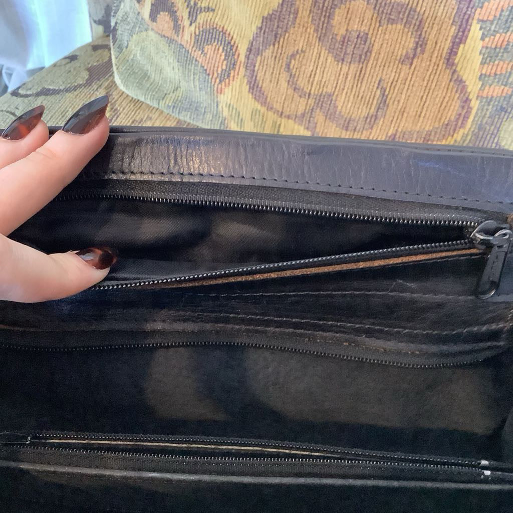 Black leather handbag with a hand holding it open, on a patterned fabric background