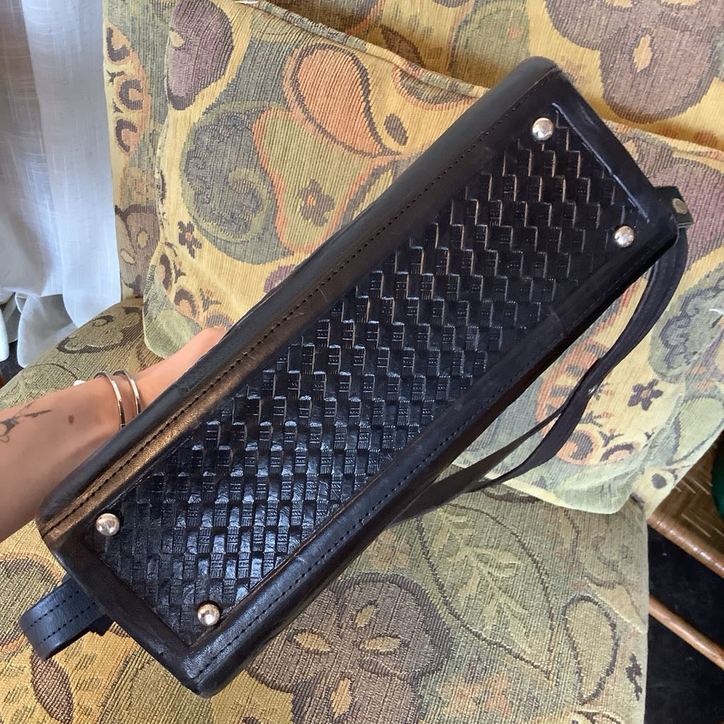 Black woven clutch bag held by a hand on a patterned fabric background