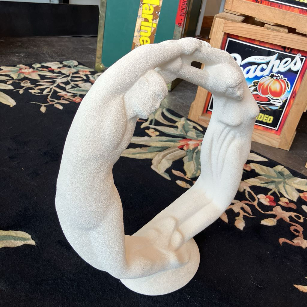 White sculpture of two figures embracing on a dark surface with decorative elements in the background.