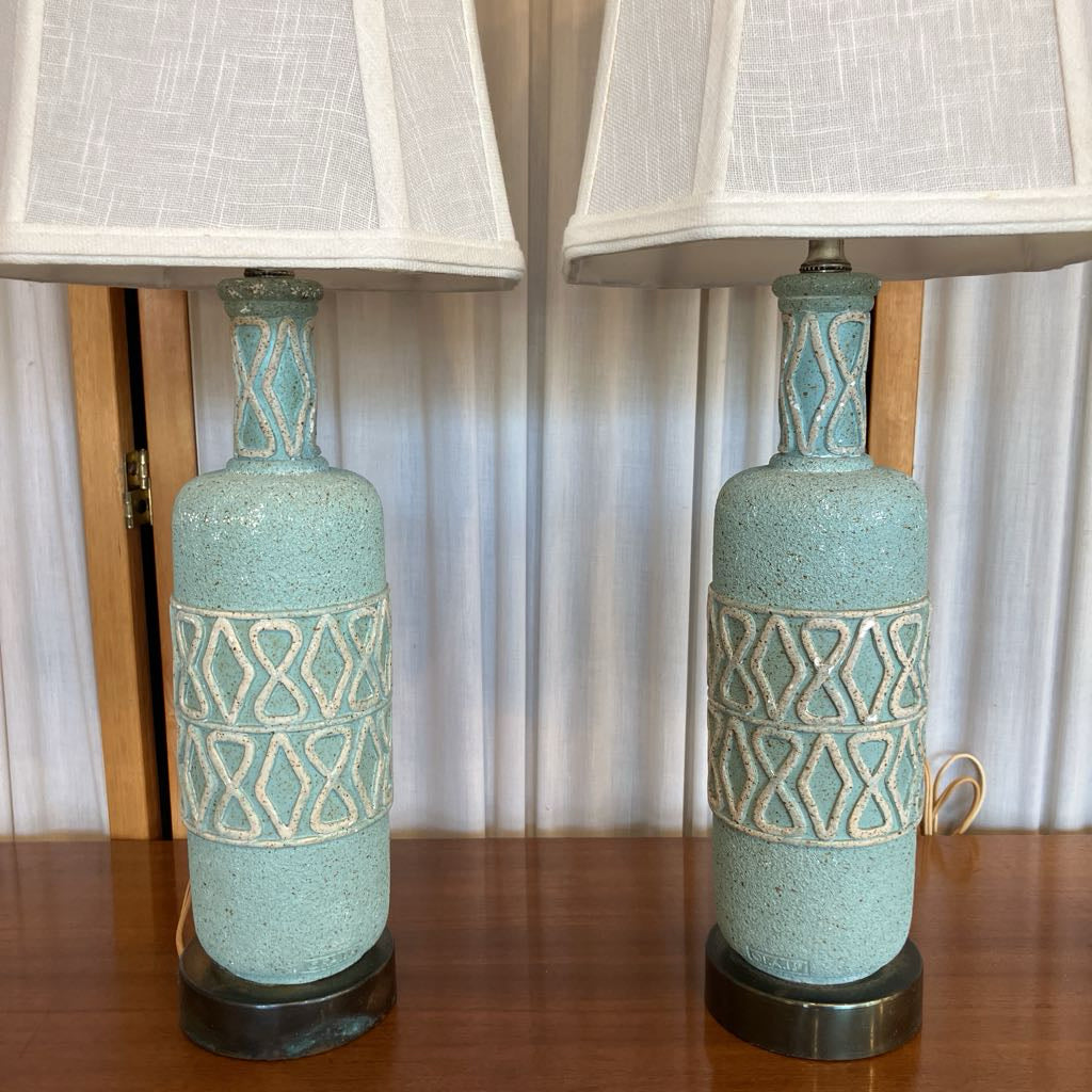 Two turquoise ceramic lamps with white lampshades on a wooden surface.