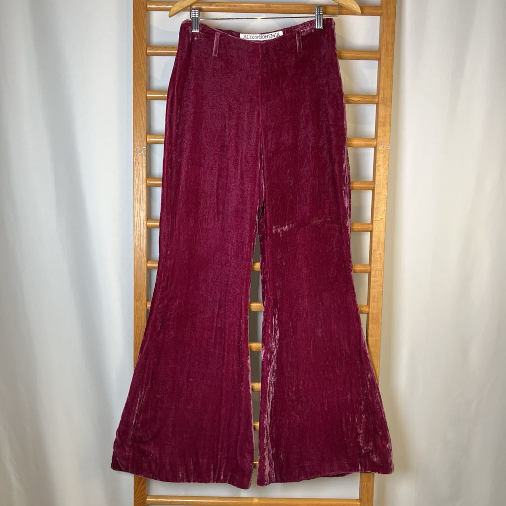 Maroon velvet flared pants hanging on a wooden rack against a white background