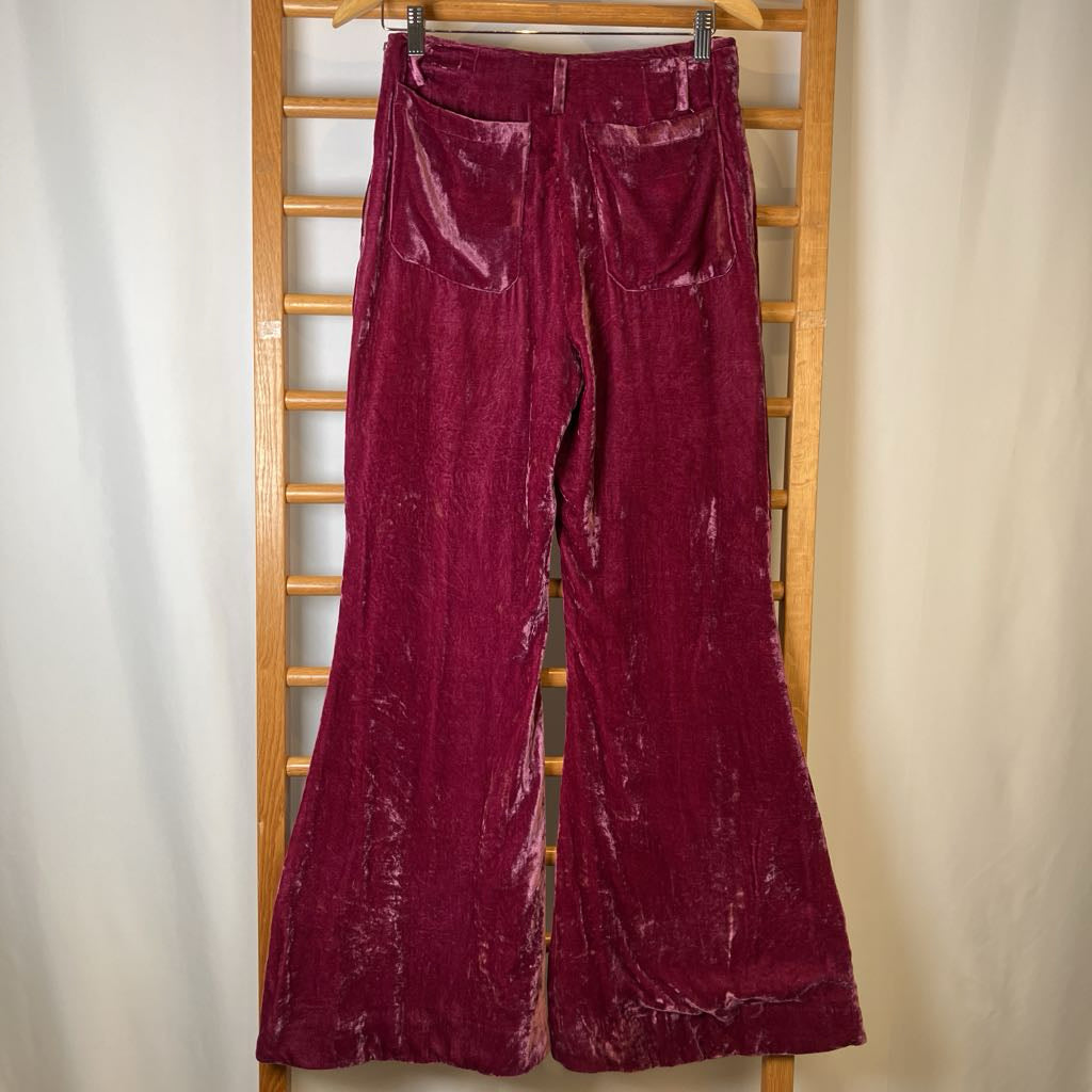Maroon velvet bell-bottom pants hanging on a wooden rack against a neutral background