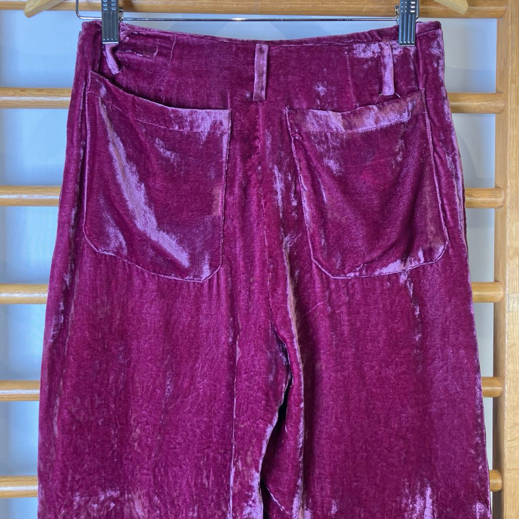Purple velvet pants hanging on a wooden rack.