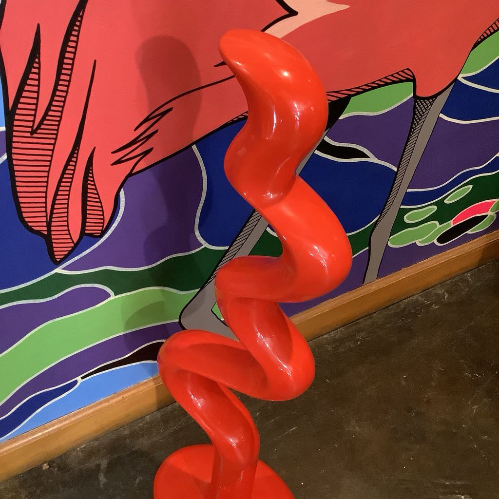 Red spiral sculpture in front of a colorful abstract mural