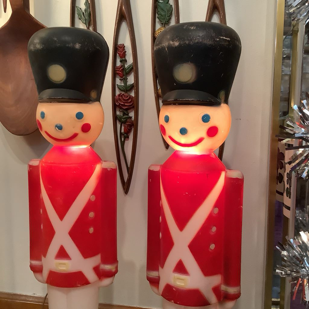 Two illuminated toy soldier figures with red uniforms and black hats in a store setting.