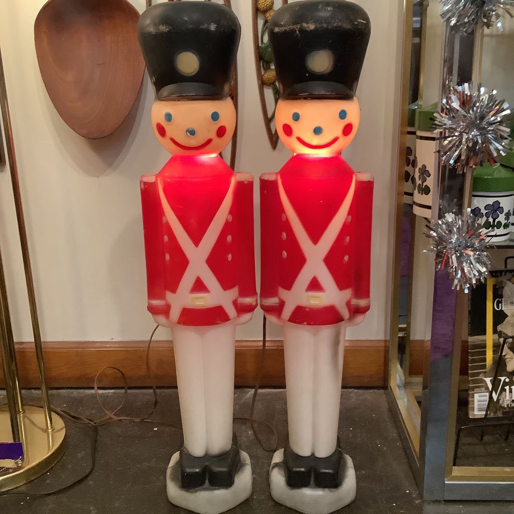 Two toy soldier figurines with red suits and black hats in a room setting.