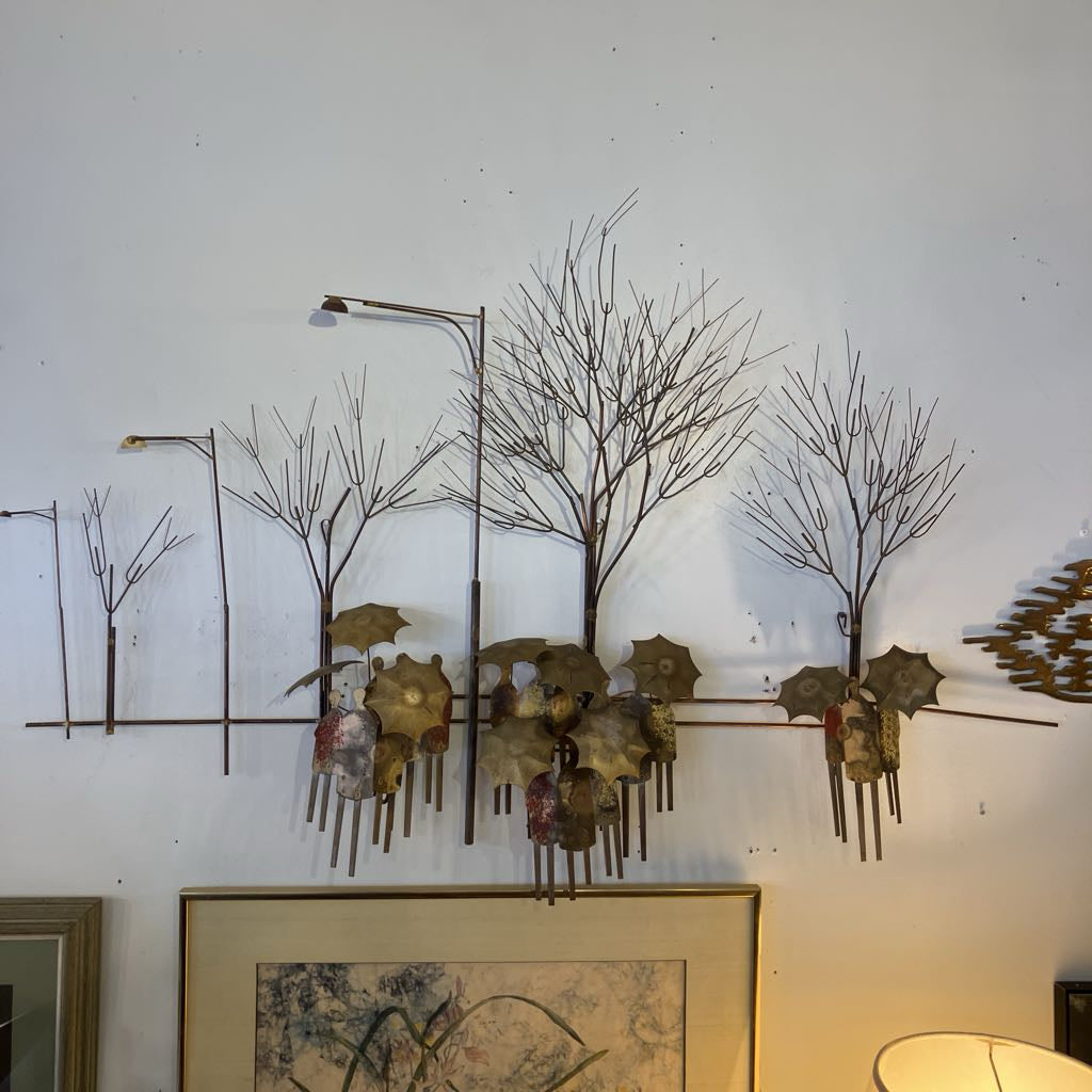 Metal wall art of trees and people with umbrellas on a white wall