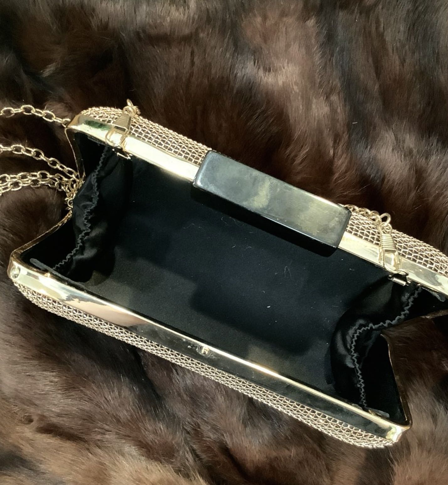 Black clutch with gold chain on a fur surface