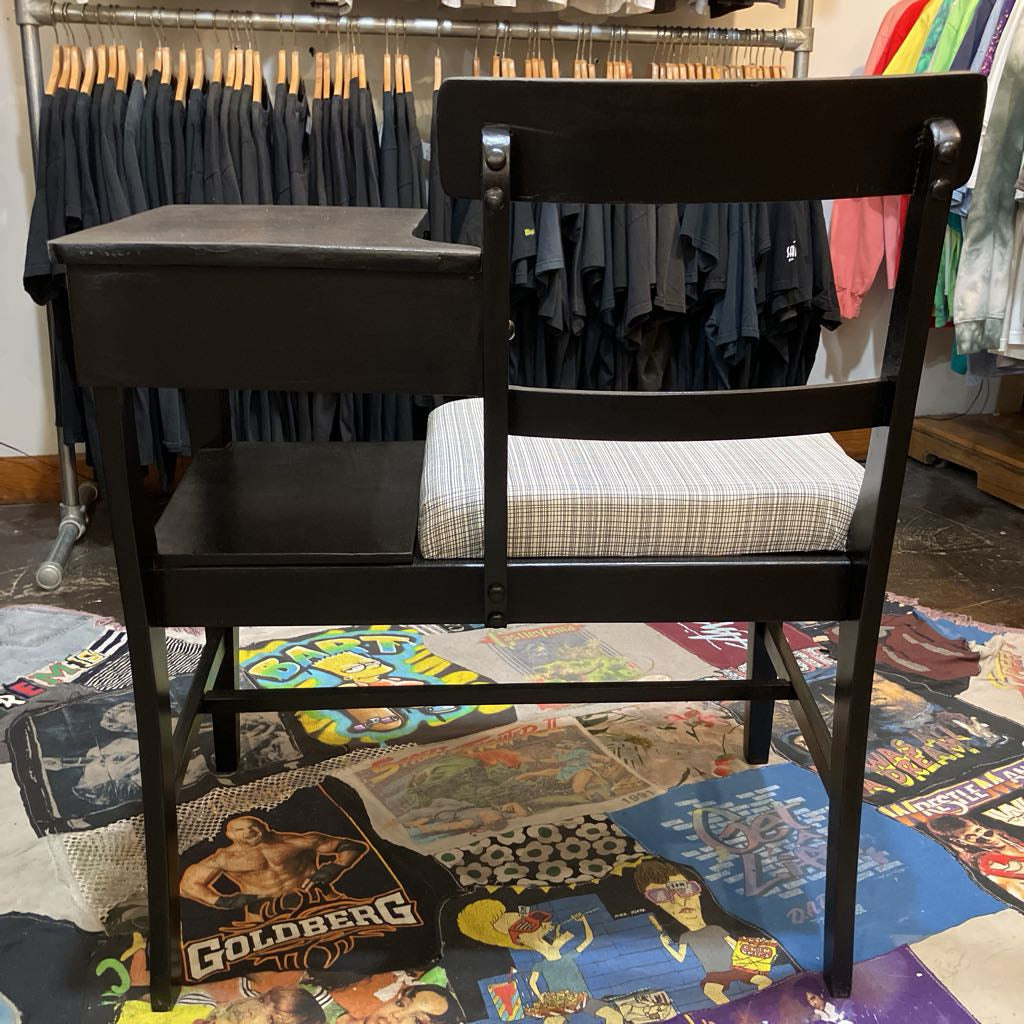 Black chair with a cushioned seat in a room with clothing racks and a colorful rug.
