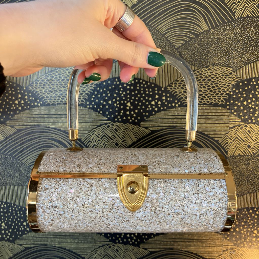 Silver glittery handbag with gold accents held by a hand against a patterned background