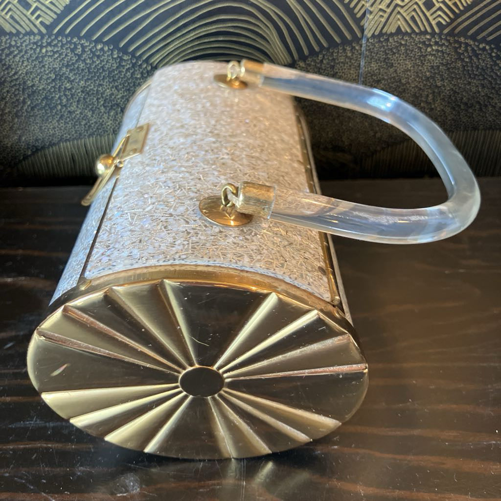 Decorative metal box with gold lid and clear handle on a dark surface