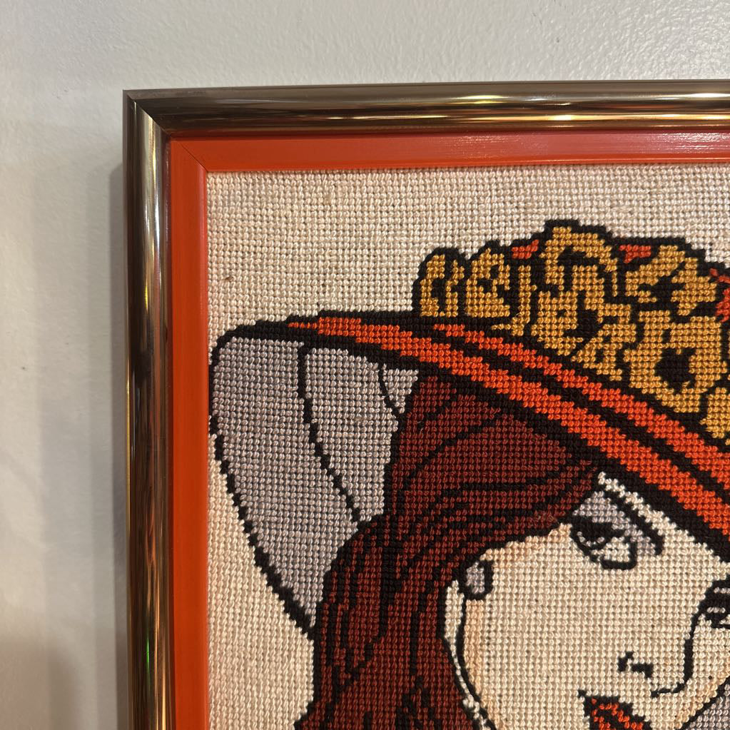 Close-up of a cross-stitched portrait with a decorative frame.