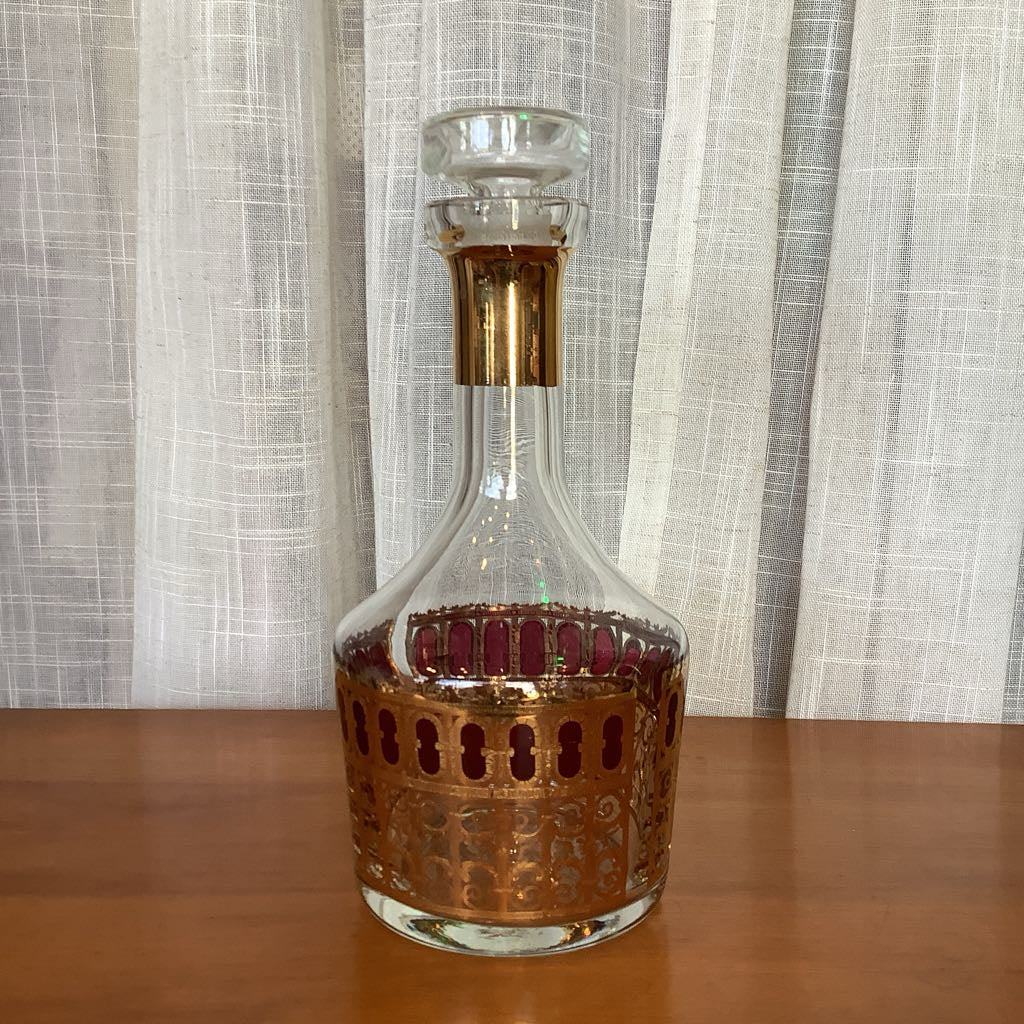 Decorative glass decanter with gold accents on a wooden surface and light curtain background