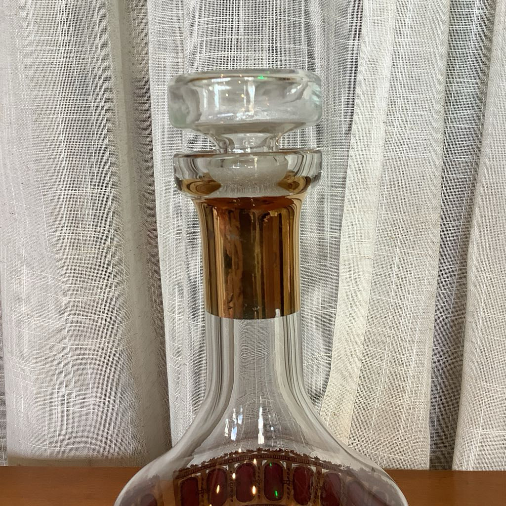 Glass decanter with a gold stopper on a wooden surface with a light curtain background