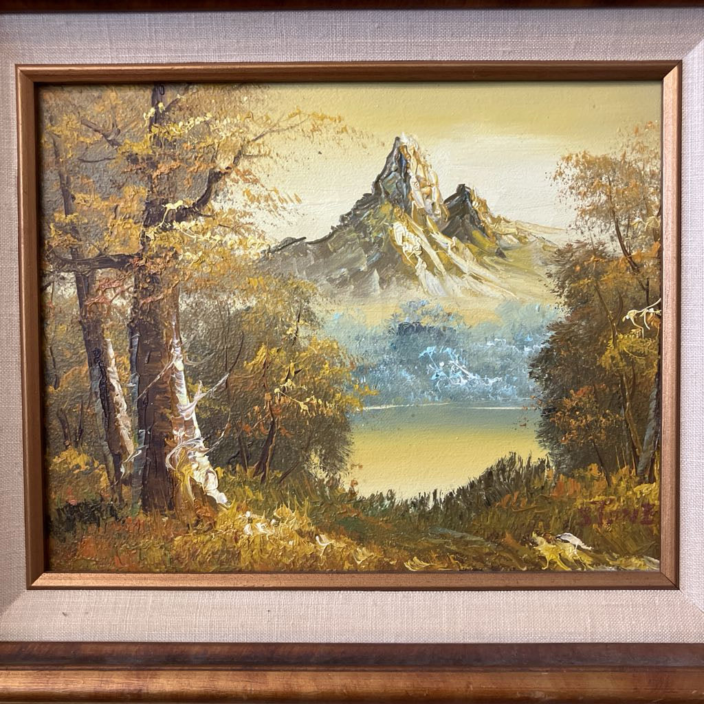 Painting of a mountain landscape with trees and a lake, framed in brown.