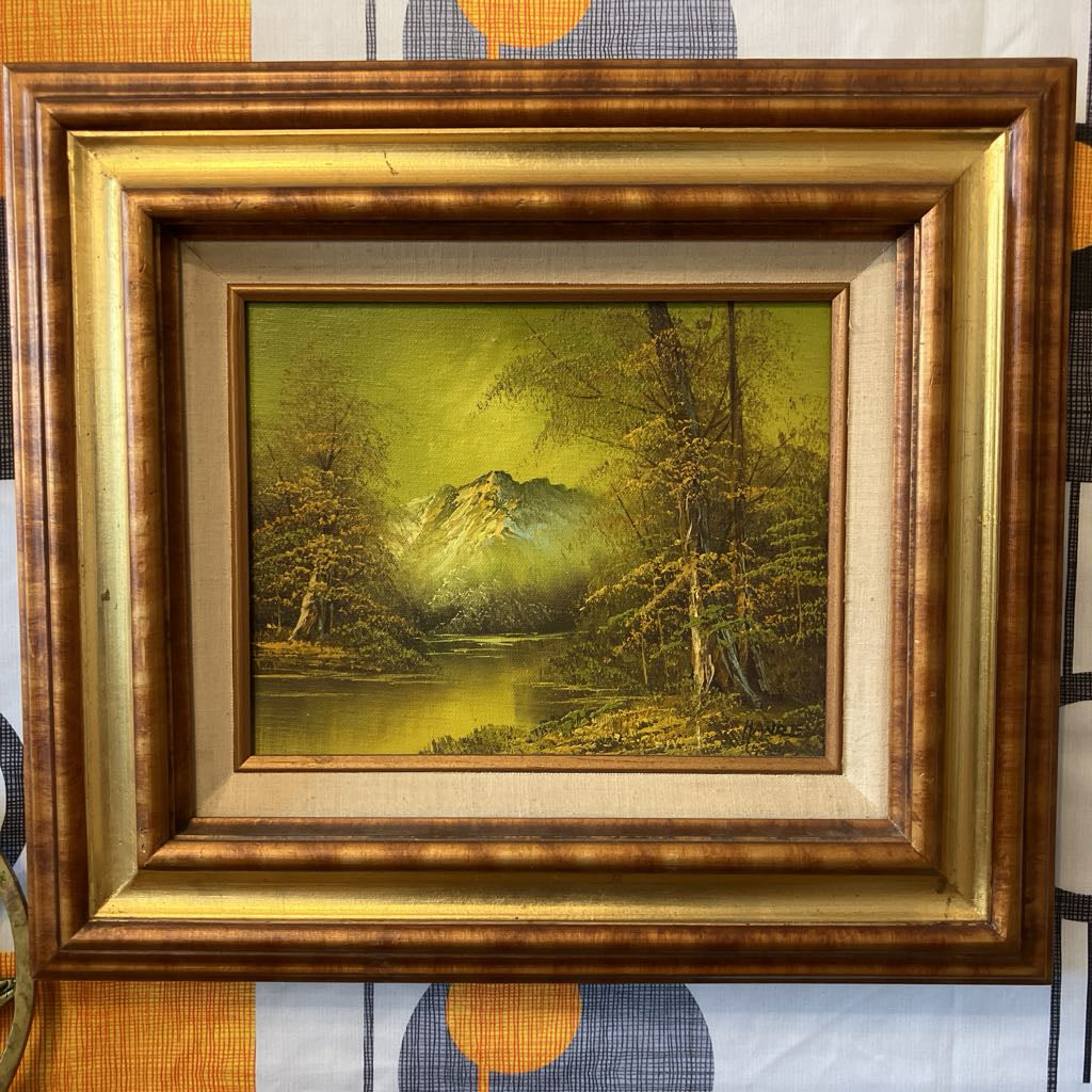 Framed painting of a landscape with trees and mountains.