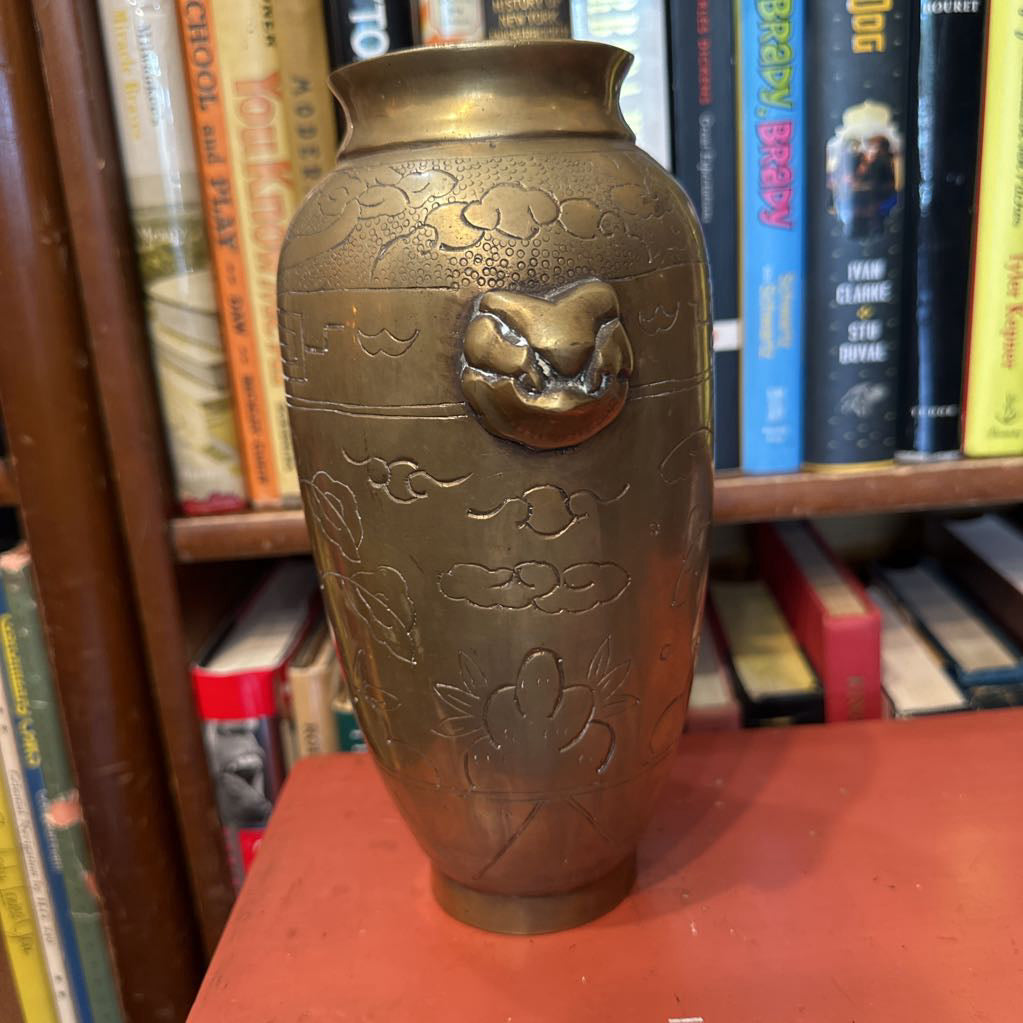 Bronze vase with embossed designs on a bookshelf
