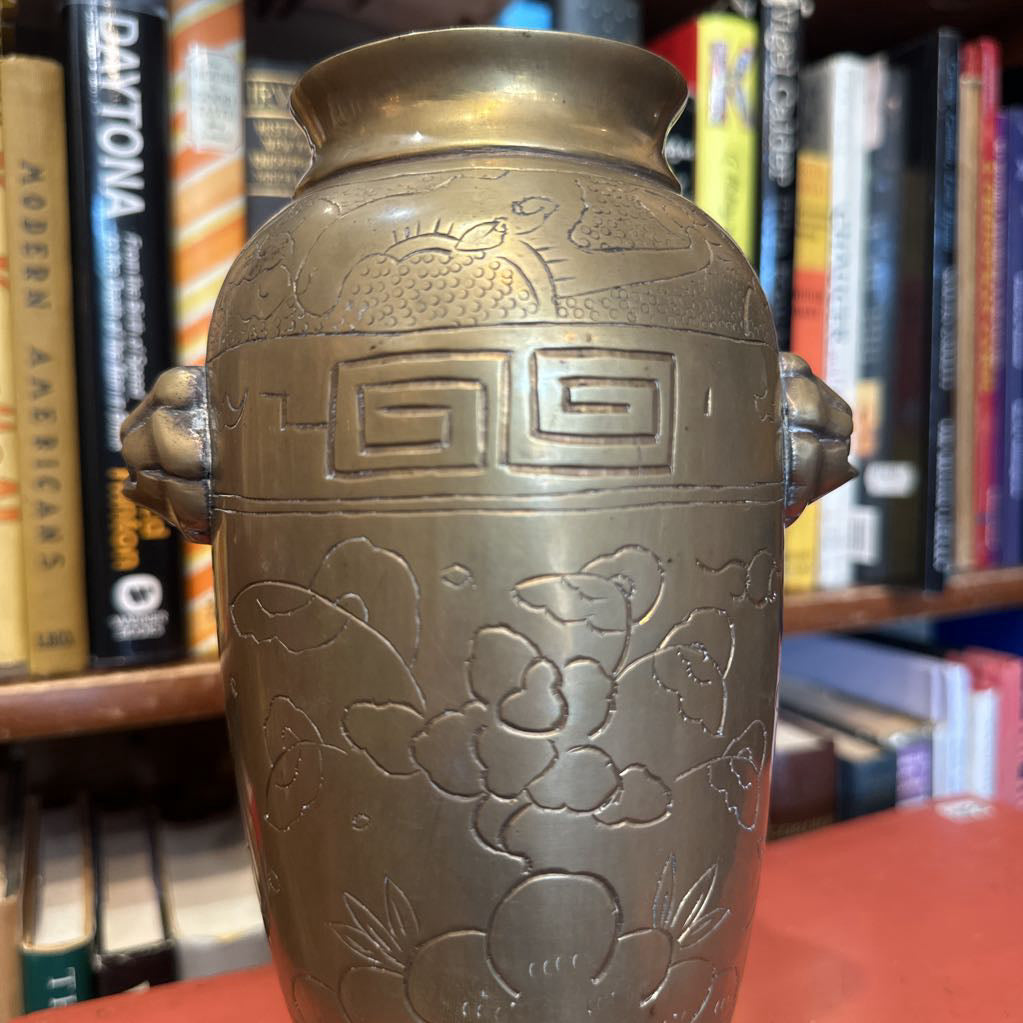 Bronze vase with floral designs in front of a bookshelf