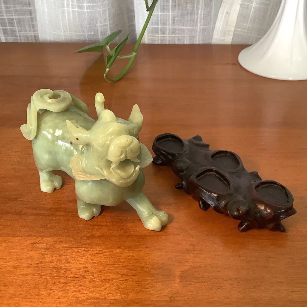 Green ceramic dragon figurine and black metal knuckle duster on a wooden surface.