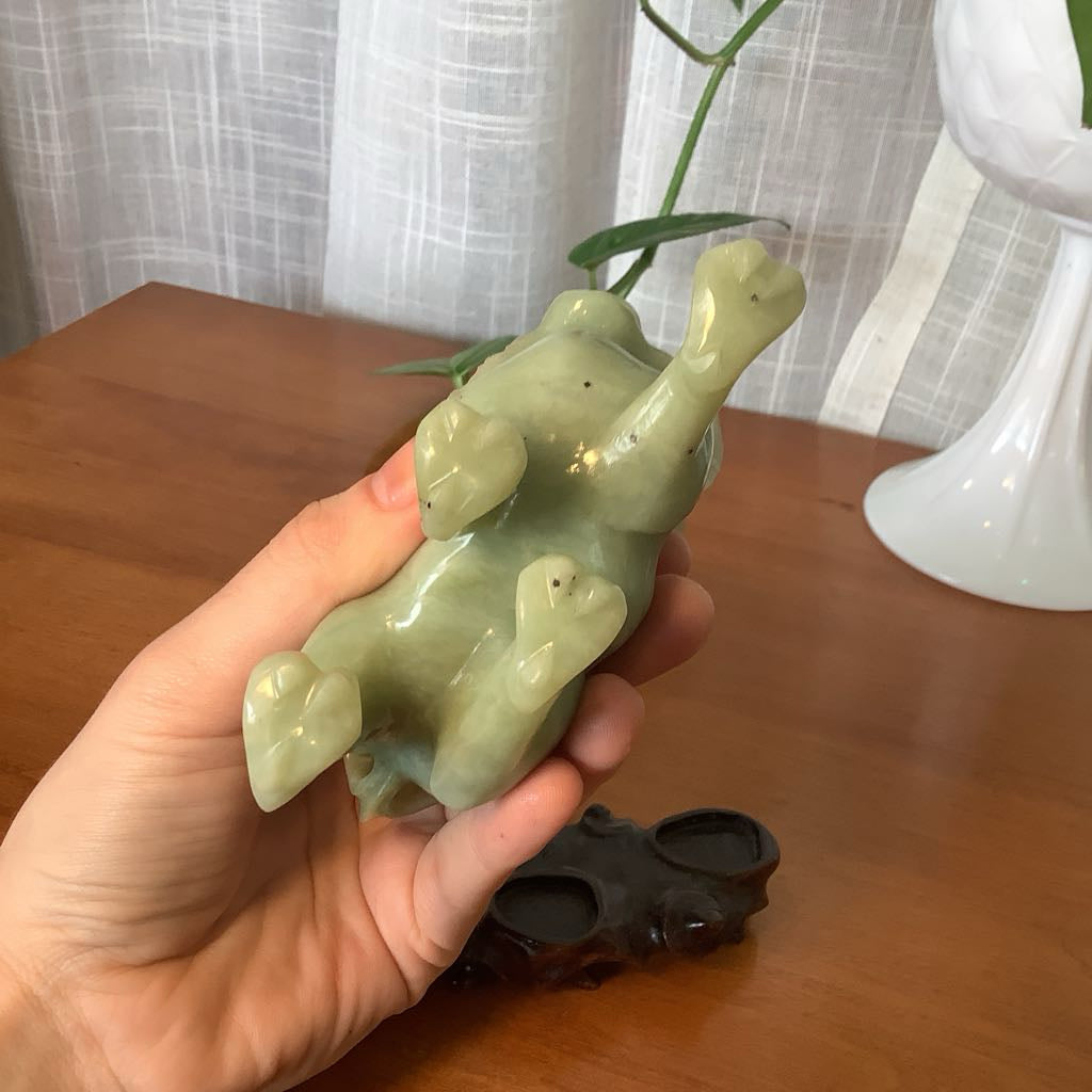 Hand holding a green ceramic dog figurine on a wooden surface with a white curtain in the background.