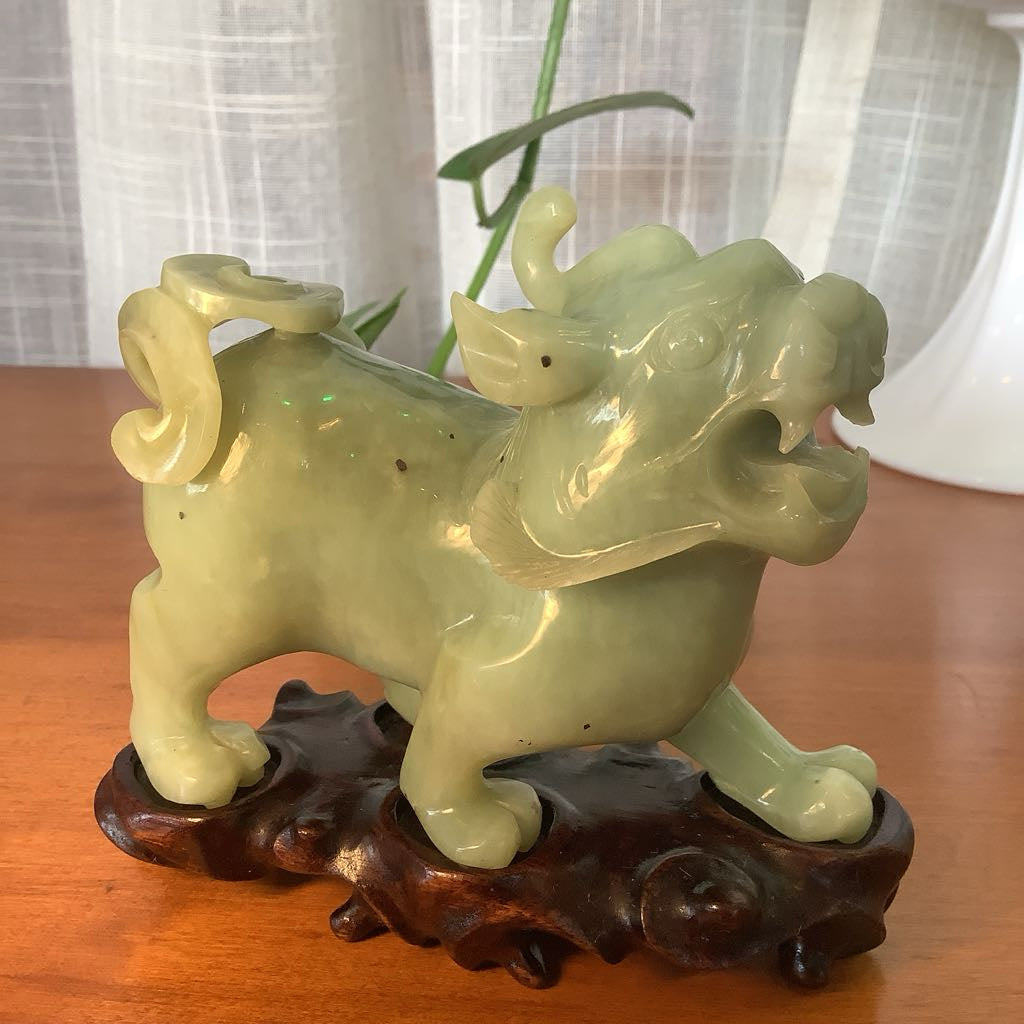 Green ceramic dragon figurine on a wooden base with a blurred background