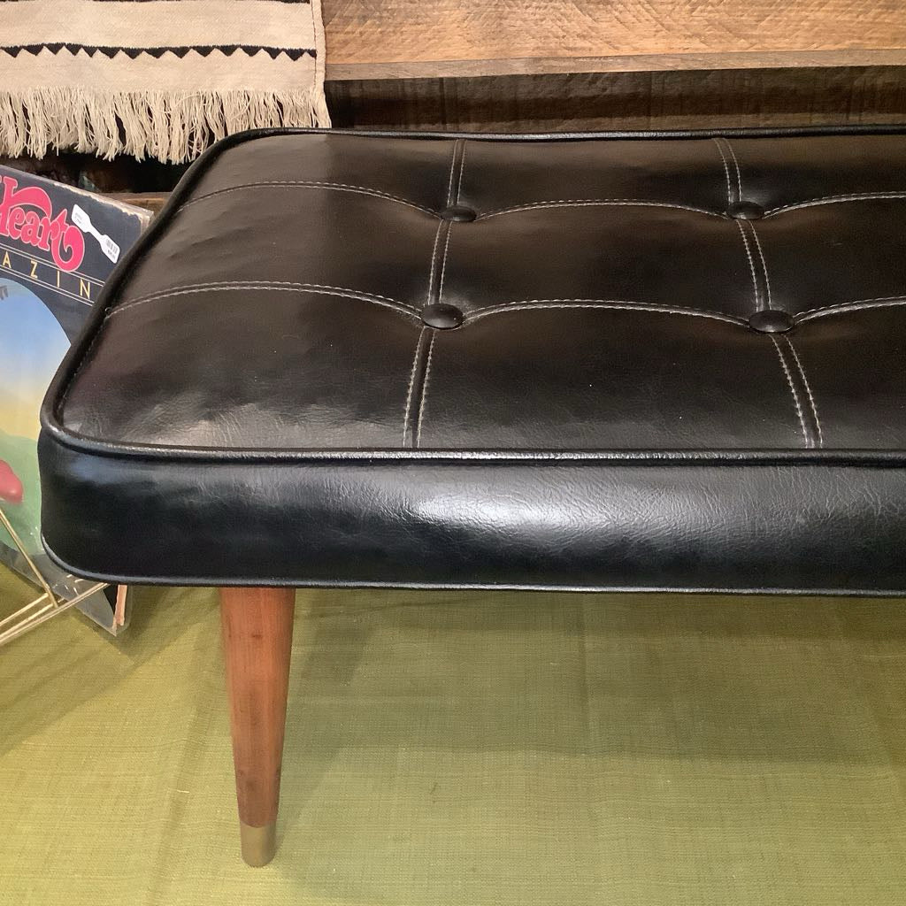 Black leather bench with wooden legs on a green floor.