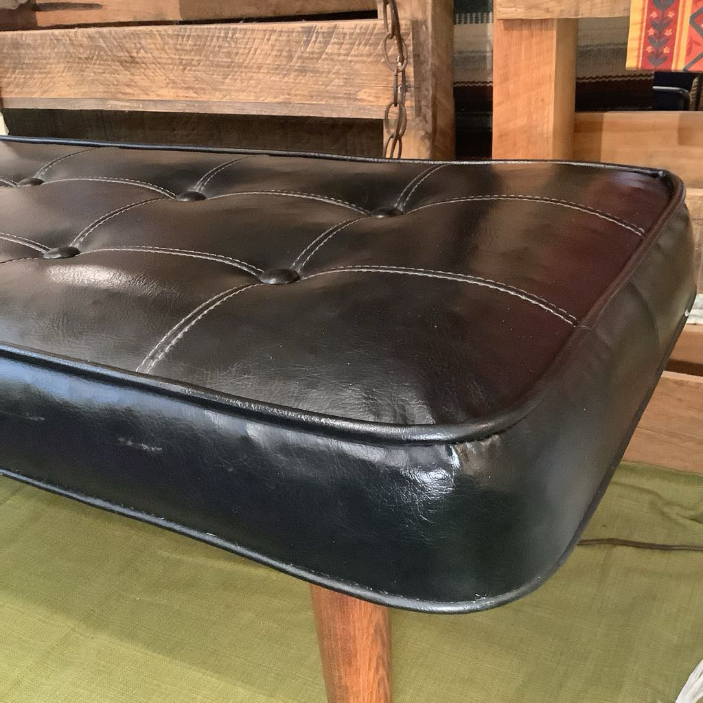 Black leather ottoman with wooden legs on a green surface