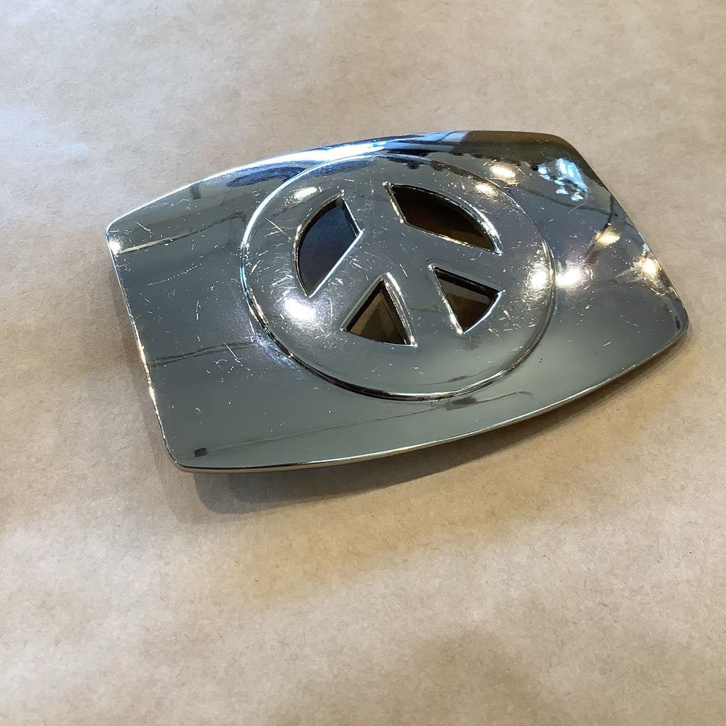 Chrome belt buckle with peace symbol on a beige background