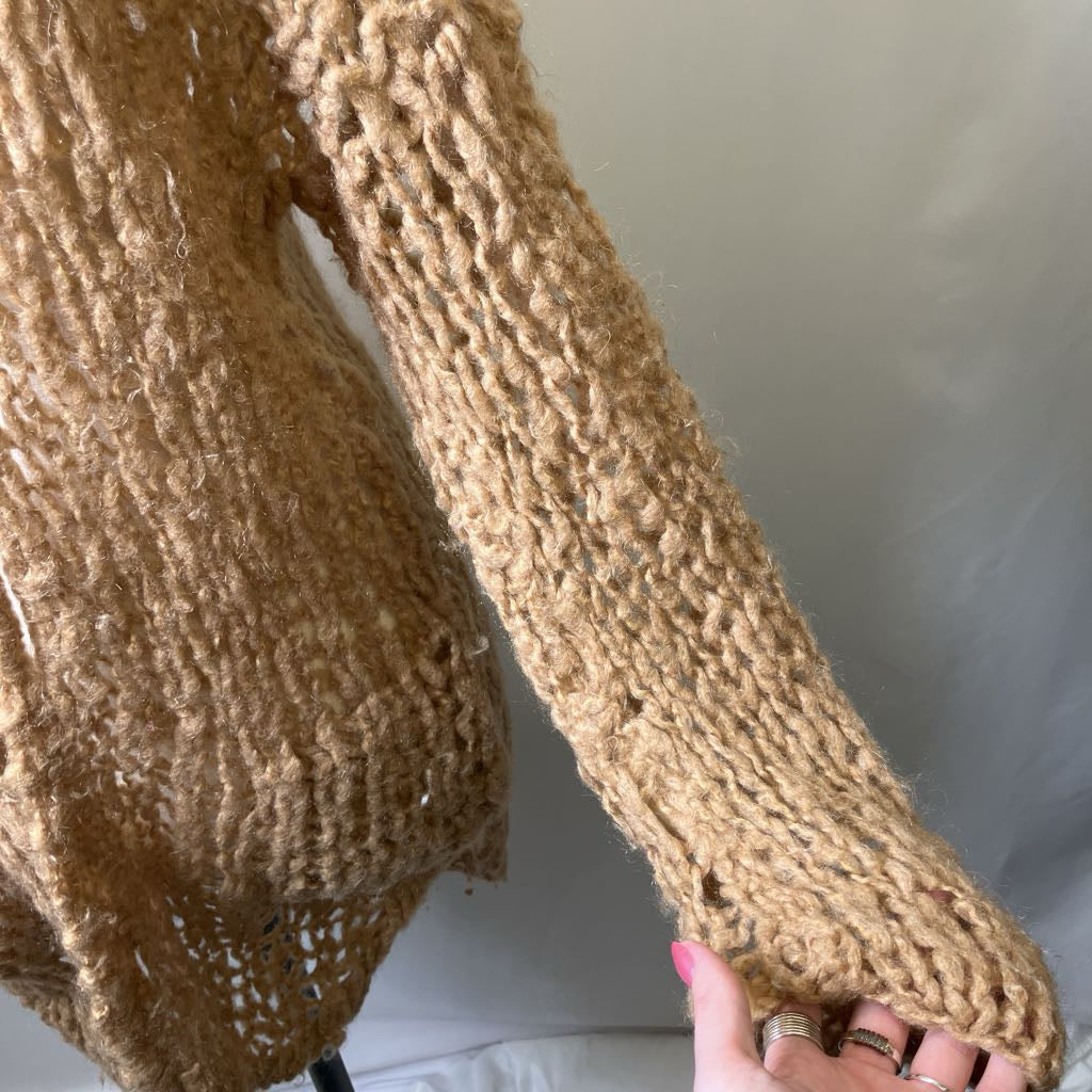 Close-up of a brown knitted sweater sleeve with a hand wearing rings.