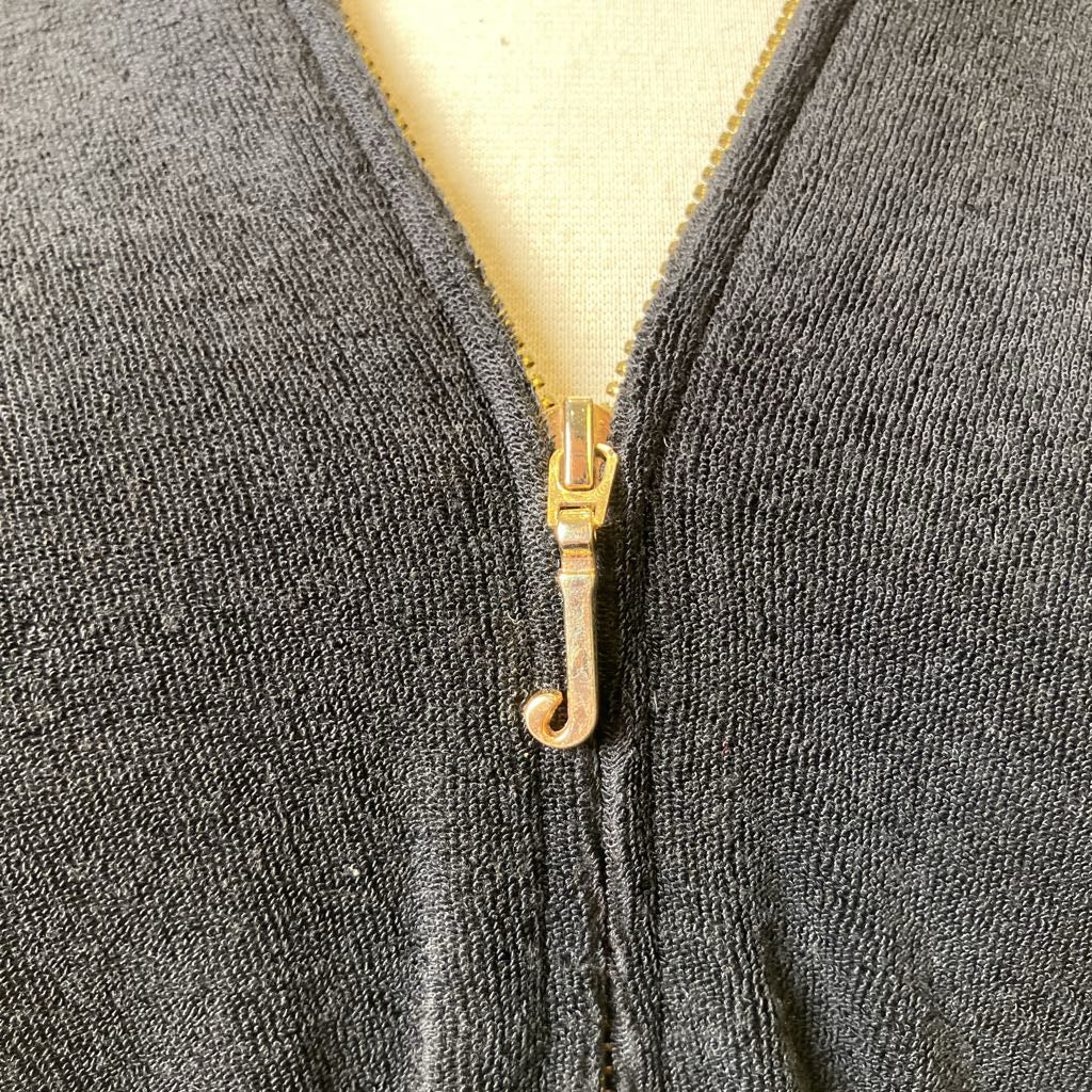 Close-up of a gold J zipper on a black textured fabric