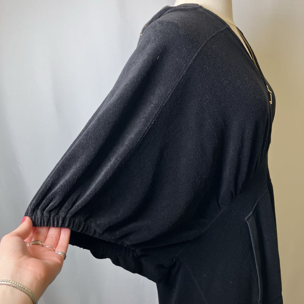 Black garment on a mannequin with a hand adjusting the sleeve against a neutral background