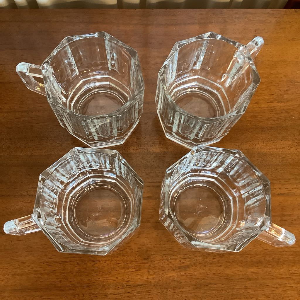 Four clear glass mugs with handles on a wooden surface