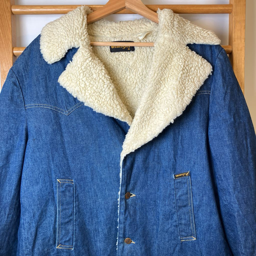 Blue denim jacket with cream sherpa lining hanging on a wooden rack.